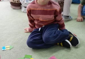 chłopiec siedzi na dywanie przed nim leżą figury geometryczne