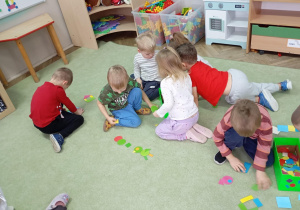 dzieci siedzą na dywanie przed nimi leżą figury geometryczne