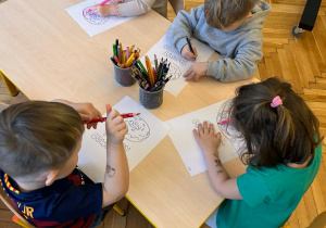 dzieci siedzą przy stoliku i kolorują kolorowankę