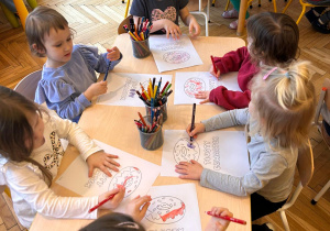 dzieci siedzą przy stoliku i kolorują kolorowankę