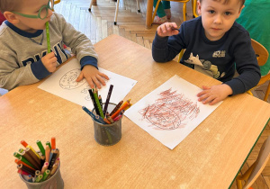 dzieci siedzą przy stoliku i kolorują kolorowankę