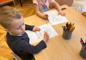 dzieci siedzą przy stoliku i kolorują kolorowankę