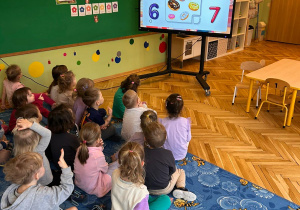 grupa dzieci siedzi przed ekranem multimedialnym