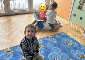 na pierwszym planie siedzi dziewczynka, na drugim planie grupa dziewczynek ogląda książeczki