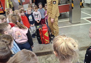 strażak prezentuje dzieciom sprzęt strażacki w kształcie plecaka