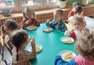 dzieci siedzą przy stoliku i jedzą frytki