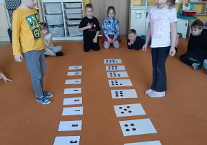 chłopiec i dziewczynka stoją przed kartkami ułożonymi w dwóch rzędach na przeciwko siebie