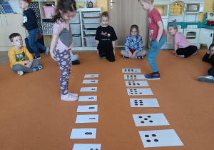 dwoje dzieci porusza się przed kartami z cyframi i kropkami