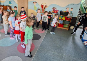 Dzieci stoją w kolejce i kopią piłkę do bramki