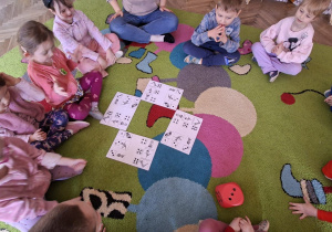 dzieci siedzą w kole, rzucają kostką i patrzą na karty z gimnastycznymi figurami