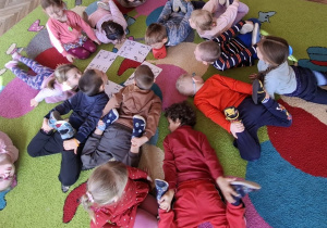 grup dzieci kładzie się na dywanie na brzuchu podnosząc nogi nad podłogę