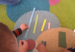 kolorowe paski różnej długości i ręce dziecka układającego patyczki
