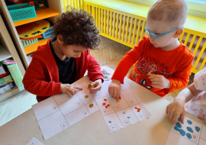 chłopcy przyklejają kawałki plasteliny na kartkę