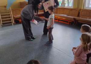 pani wykonuje uścisk dłoni dziewczynce i gratuluje a pani dyrektor trzyma grę planszową