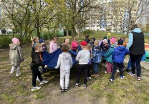 dzieci stoją w ogrodzie przedszkolnym, trzymają chustę