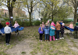 dzieci stoją w ogrodzie przedszkolnym, trzymają chustę