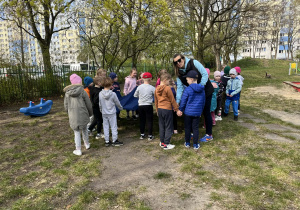 dzieci stoją w ogrodzie przedszkolnym, trzymają chustę
