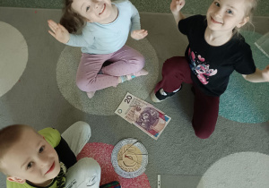 dzzieci siedzą na dywanie przed nimi leżą pieniądze