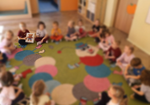 dzieci siedzą w kole, chłopiec trzyma obrazek misia