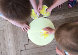 dzieci układają na żółtym kole wycięte z papieru dłonie