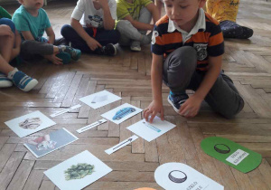 dziecko układa obrazek na podłodze a za nim siedzi grupa dzieci