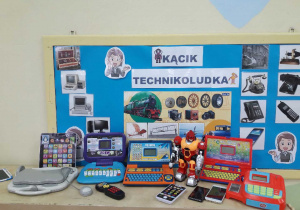 tablica z obrazkami urządzeń technologicznych oraz zabawkowe laptopy, kasa, telefony.