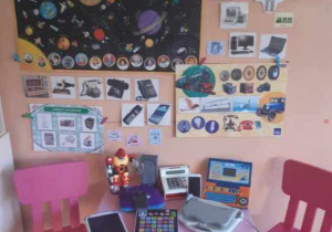 na ścianie wisza obrazi z urządzeniami technologicznymi i kosmosem oraz na stoliku zabawkowe laptopy.