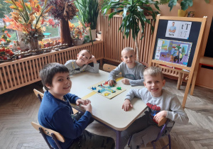 czterech chłopców siedzi przy stoliku i gra w chinczyka