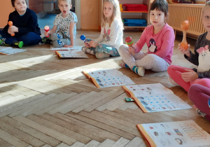 grupa dzieci siedząca na podłodze przed książkami i gra na instrumentach muzycznych