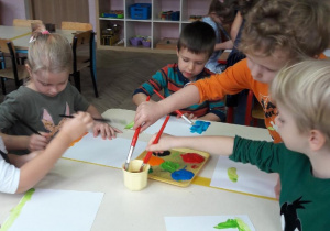 grupka dzieci maluje farbami po kartkach
