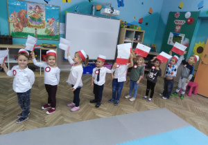 9 dzieci stoi jedno za drugim machając flagami biało-czerwonymi nad głowami