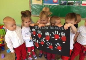 rrupa dzieci stoi obok siebie i trzyma plakat "Jesteśmy Polakami" z łapkami biało-czerwonymi