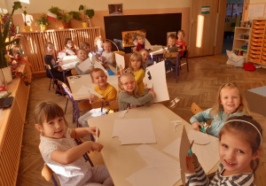 Dzieci siedzą przy stolikach i wykonują pracę plastyczną