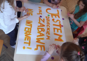 grupa dzieci ozdabia plakat z napisem "Jestem dzieckiem wolę zabawę nie Internet".