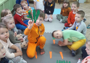 chłopiec w środku koła trzyma sylwetę natki marchewki a w koło siedzą dzieci
