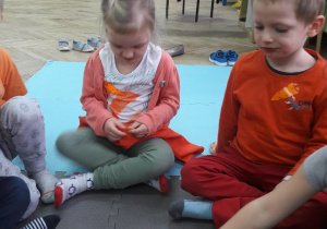 dziewczynka trzyma w rączkach marchewkę, obok siedzi chłopiec a przed nimi stoi talerz z pokrojoną na kawałeczki marchewką