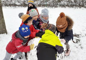 grupka dzieci toczy wielka kolę śniegową