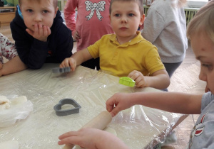 dzieci przy stole z foremkami a dziewczynka z prawej strony wałkuje ciasto