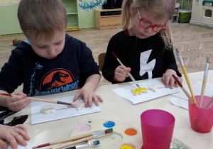 dwoje dzieci maluje farbami kształty z masy solnej