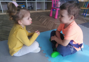 Dwoje dzieci siedzi naprzeciwko siebie twarzami pokazując miny