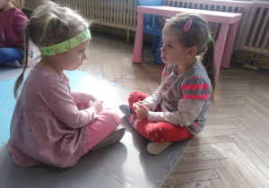 dwie dziewczynki siedzą naprzeciwko siebie i pokazują mimiką smutek