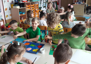 grupa dzieci maluje farbami wiosnę na białych kartonach