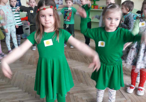 dwie dziewczynki w zielonych sukienkach machają rękoma