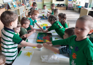 duża grupa dzieci przy długim stole maluje farbami