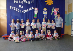 grupa dzieci z nauczycielką na tle dekoracji pasowania na przedszkolaka