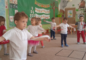 Dzieci stoją w grupie i wykonują zadana ruchowe.