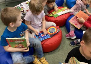 Dzieci siedzą na dywanie w bibilotece i przeglądają książki