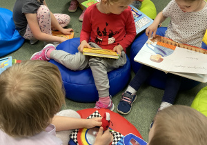Dzieci siedzą na dywanie w bibilotece i przeglądają książki.