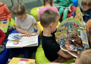 Dzieci siedzą na dywanie w bibilotece i przeglądają książki.