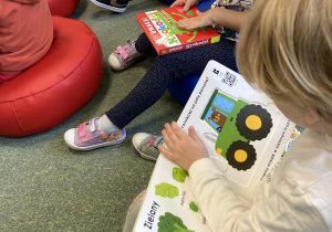 Dzieci siedzą na dywanie i wspólnie oglądają książki